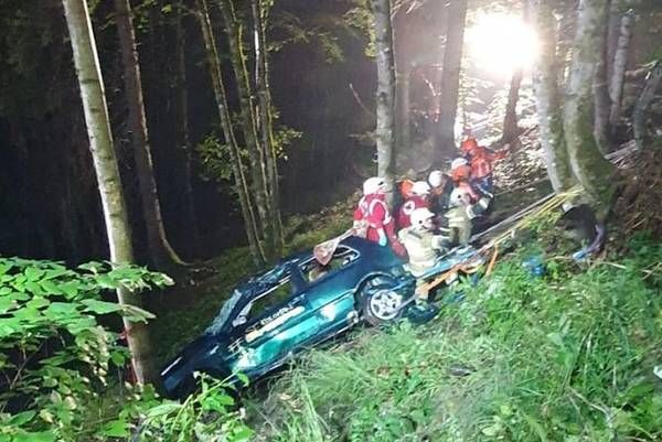 Rescuers work at the site of a car accident in a forest area. Emergency personnel in red and white uniforms assist a car that has veered off the road.