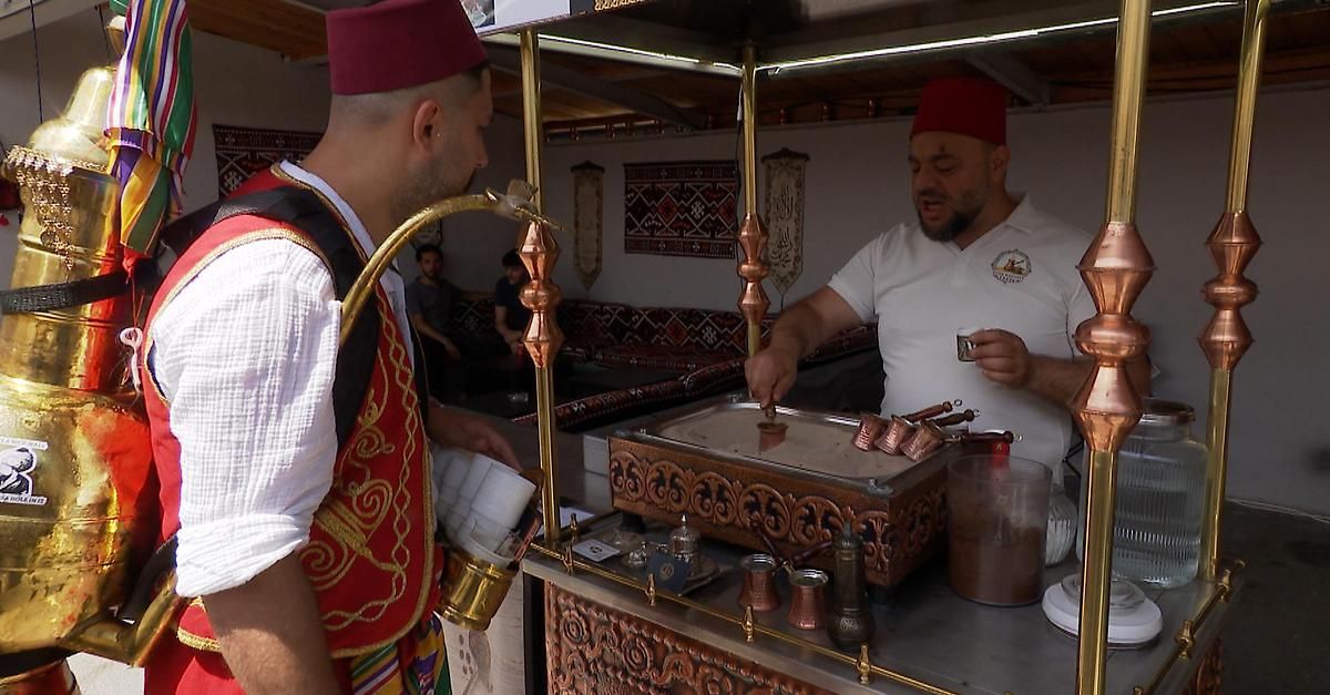 Zwei Männer bereiten Getränke in einem Marktstand zu. Einer trägt einen roten Fez und hält eine Kanne, der andere in einem weißen Hemd hält einen Becher.