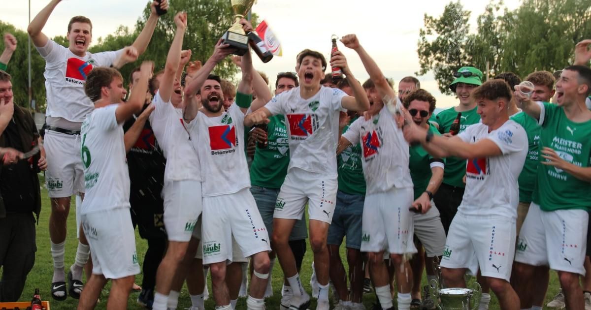 A soccer team celebrates their victory with a trophy and drinks, surrounded by cheering teammates in a grassy field.