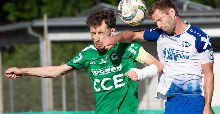 Zwei Fußballspieler konkurrieren; einer blockt einen Ball in der Luft, während der andere zusieht.