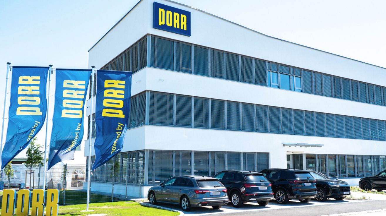 Ein modernes Bürogebäude mit blauen Fenstern und dem Wort PORR auf dem Dach. Autos davor geparkt.