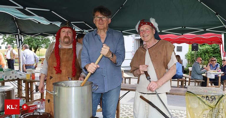 Three men, one cooking, one smiling, and one holding a knife, dressed in medieval attire, standing under a tent.
