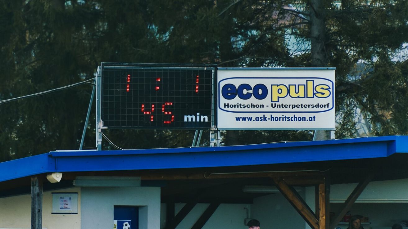 A scoreboard displays a time of 1:45, and an advertisement for Eco Pulse is mounted above it. Trees and a building are visible in the background.