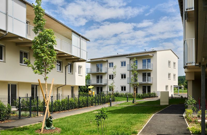 A view of a modern housing complex with several buildings and green lawns. Trees and bushes are planted in the front yard.