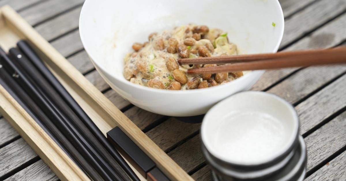 Eine Schüssel mit Tofu und Chopsticks auf einem Holztisch, begleitet von einer kleinen Schüssel mit einem Löffel.