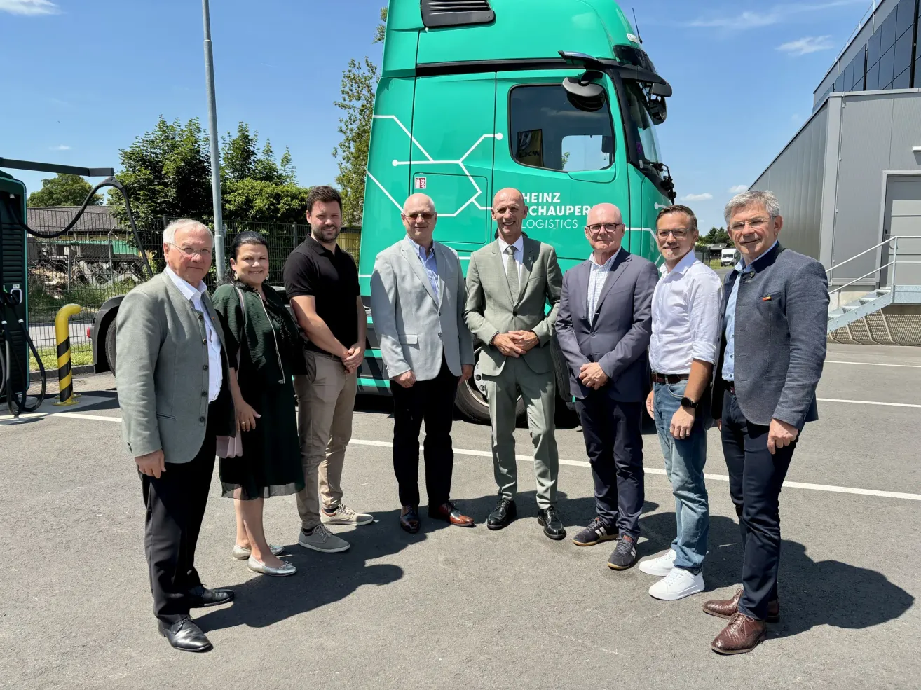 A group of men and women stand in front of a Heinz Chauper Logistics truck, dressed in formal attire, and posing for a photo.