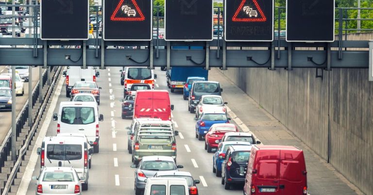 A busy highway with multiple lanes of cars and vans. Traffic signs indicate heavy traffic ahead. Vehicles are moving slowly.