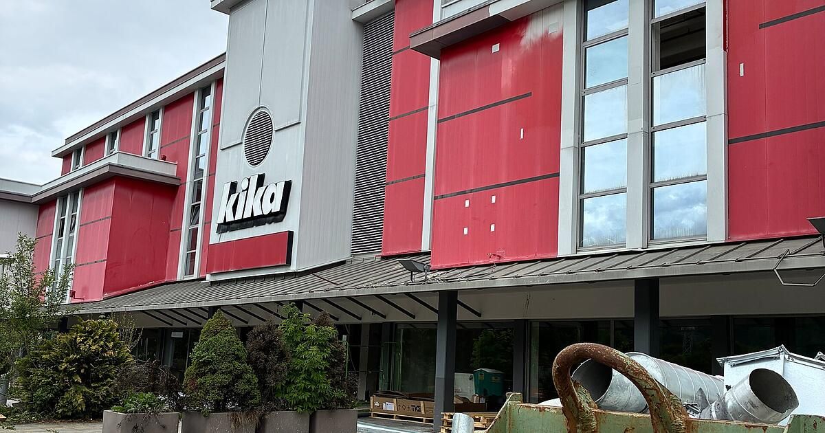 Das Äußere eines Kika-Geschäfts mit einer rot-weißen Fassade und einem prominenten Kika-Schild. Im Vordergrund befinden sich Bäume und ein Baufahrzeug.