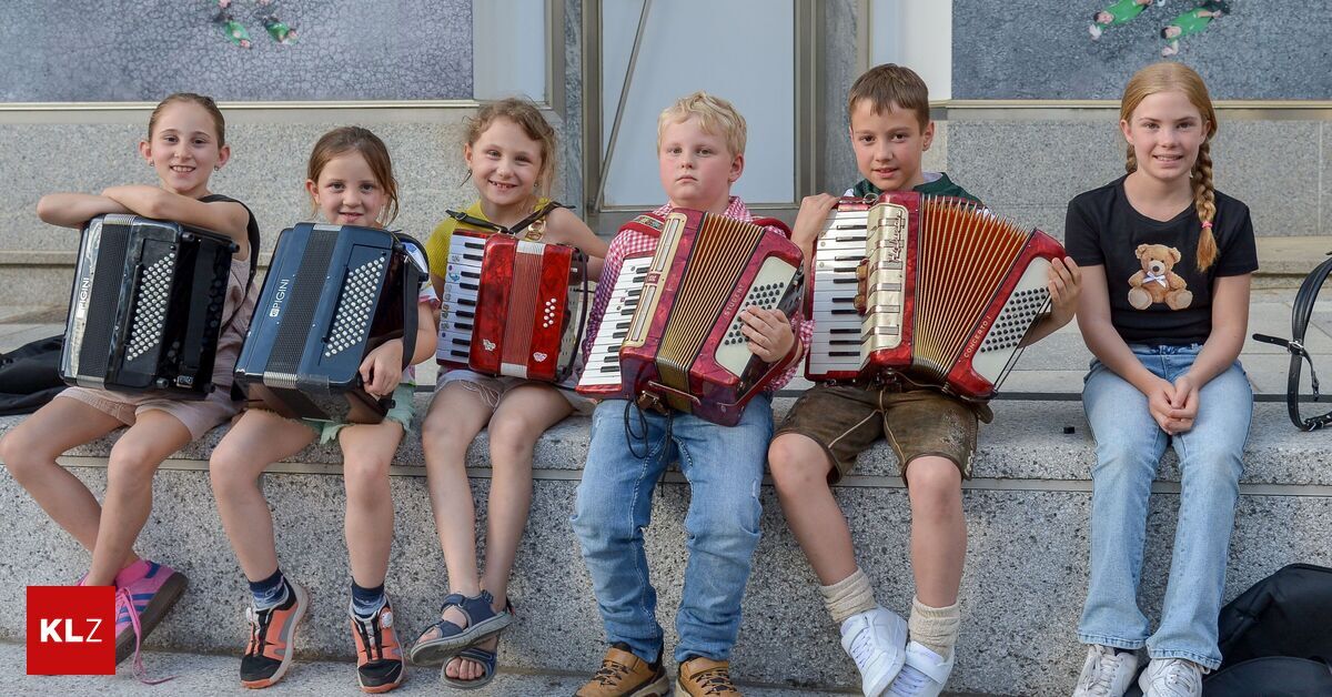 Vier Kinder sitzen auf einer Betonbank und halten Akkordeons. Sie lächeln für die Kamera. Die beiden auf der linken Seite tragen Sandalen.
