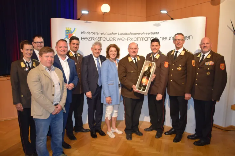 Officials from the Lower Austrian Fire Brigade Association stand with a man holding a bottle of wine in a presentation setting.