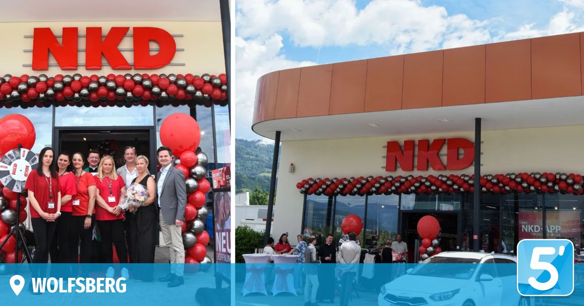 Eine Gruppe von Menschen steht vor einem Geschäft mit einer großen Ballondekoration. Ein Mann hält einen Blumenstrauß. Im Hintergrund ist ein Berg zu sehen.