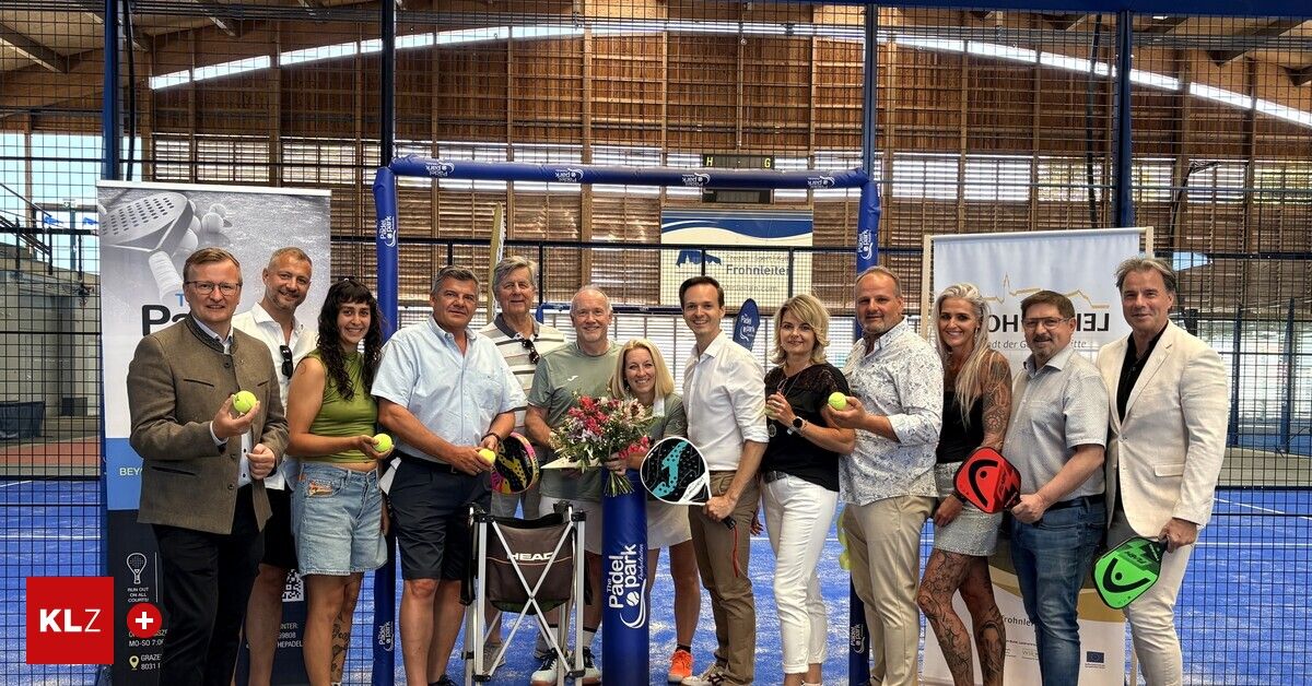 Eine Gruppe von Menschen posiert für ein Foto bei einer Sportveranstaltung, hält Tennisschläger und Tennisbälle in der Hand, mit einem blauen Tornetz im Hintergrund.