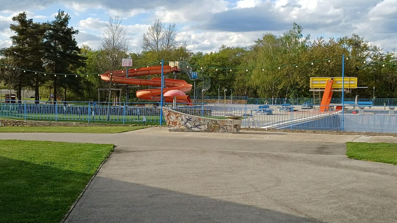 Eine leere Wasserrutsche in einem Wasserpark unter teilweise bewölktem Himmel. Bäume umgeben das Areal.