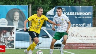 Zwei Fußballspieler, einer in einem gelben Trikot und der andere in Grün, spielen auf einem Feld. Hinter ihnen befindet sich ein Banner mit Bild und Text.