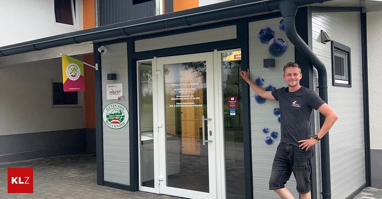 Ein Mann steht vor einem Geschäft mit Blaubeeren-Thema. Das Geschäft hat eine Glastür und ein Fenster. Der Mann trägt ein schwarzes T-Shirt.