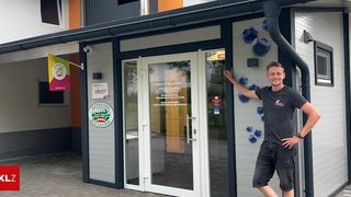 Ein Mann steht vor einem Geschäft mit Blaubeeren-Thema. Das Geschäft hat eine Glastür und ein Fenster. Der Mann trägt ein schwarzes T-Shirt.