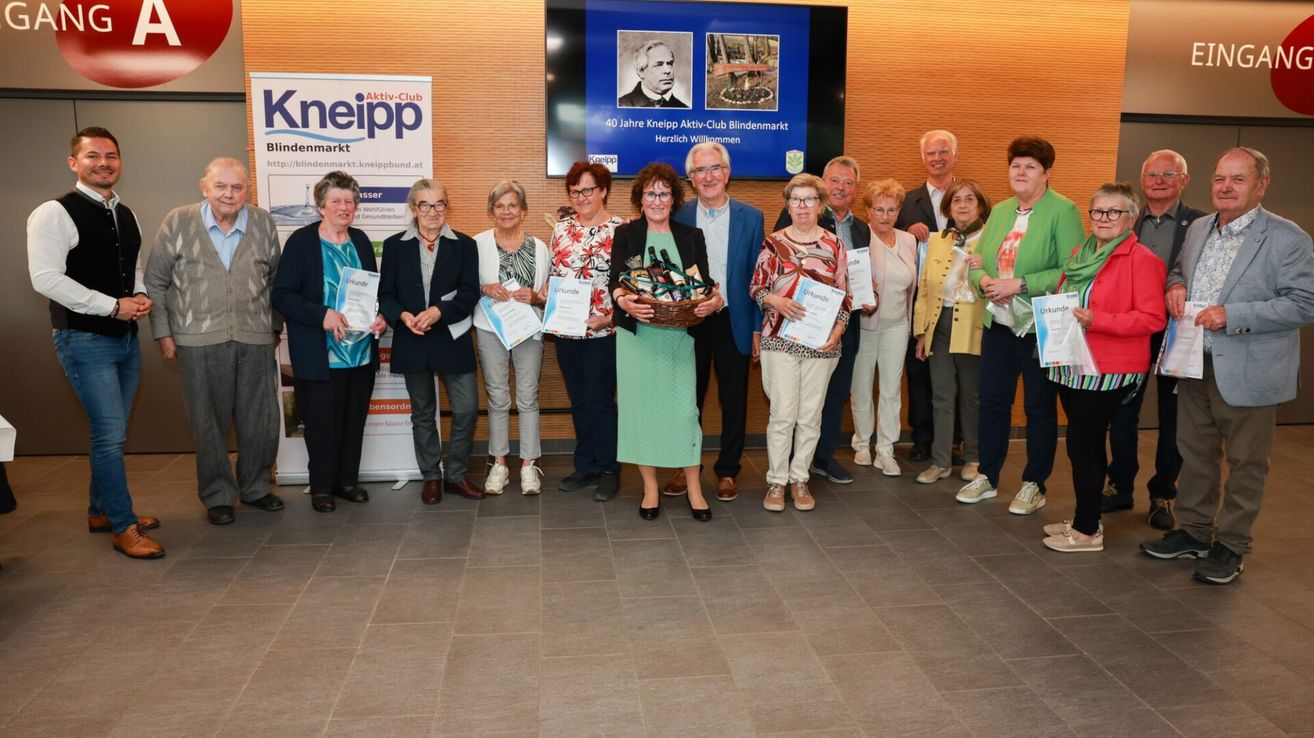 Eine Gruppe von Menschen steht zusammen, einige halten Urkunden in der Hand. Ein großer Bildschirm ist hinter ihnen mit einem Bild eines Mannes und eines Gartens. Sie sind bei der 40-Jahr-Feier des Kneipp Aktiv-Club Blindenmarkt.