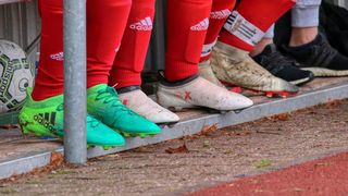 Eine Gruppe von Fußballspielern mit roten Adidas-Socken und Schuhen, einige mit grünen Akzenten, stehen auf einer Betonkante.