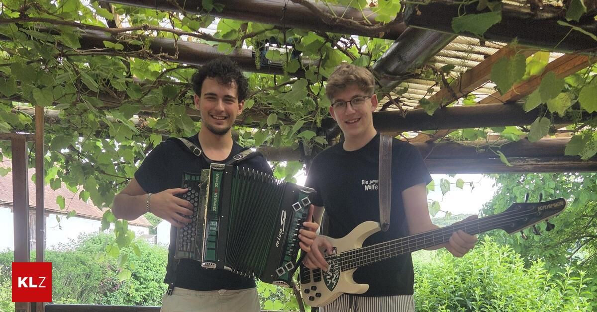 Zwei Männer stehen unter einer Laube, einer spielt Akkordeon und der andere hält eine Bassgitarre. Beide lächeln für ein Foto.