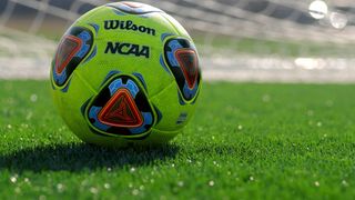 Ein grüner Wilson-Fußball mit NCAA-Marke auf einem grünen Feld. Der Ball hat rote, blaue und schwarze Designs.