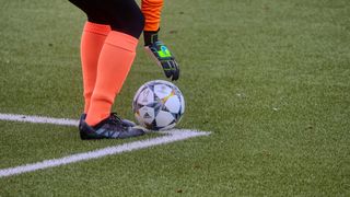 Ein Fußballspieler mit orangefarbenen Socken und schwarzen Schuhen steht kurz davor, den Champions-League-Ball auf einem grünen Feld zu treten.