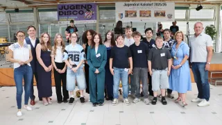 Eine Gruppe junger Menschen in einer Reihe mit einem Banner im Hintergrund mit Text und Bildern. Sie tragen Freizeitkleidung und posieren für ein Foto.