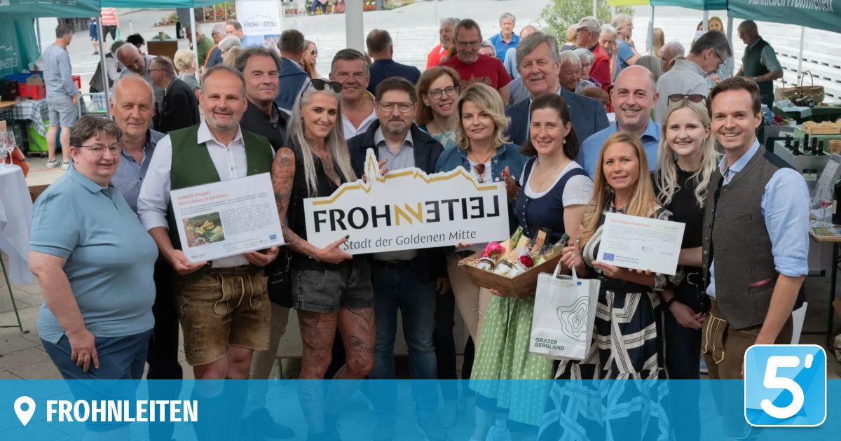 Eine Gruppe von Menschen steht zusammen, lächelt und hält Schilder und Papiere. Das Schild sagt Frohnleiten, Stadt der goldenen Mitte. Einige halten einen weißen Beutel mit grüner Schrift.