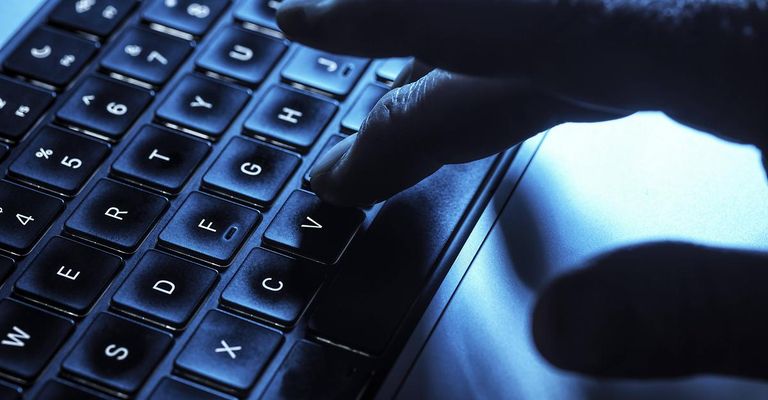 Eine Hand drückt eine schwarze Taste auf einer Laptop-Tastatur und konzentriert sich auf die 'V'-Taste. Die Tastatur ist mit einem bläulichen Schimmer beleuchtet.