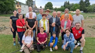 Eine Gruppe von Menschen posiert für ein Foto im Freien, einige stehen und andere sitzen auf dem Rasen. Sie alle haben Lächeln im Gesicht. Sie tragen alle Freizeitkleidung.