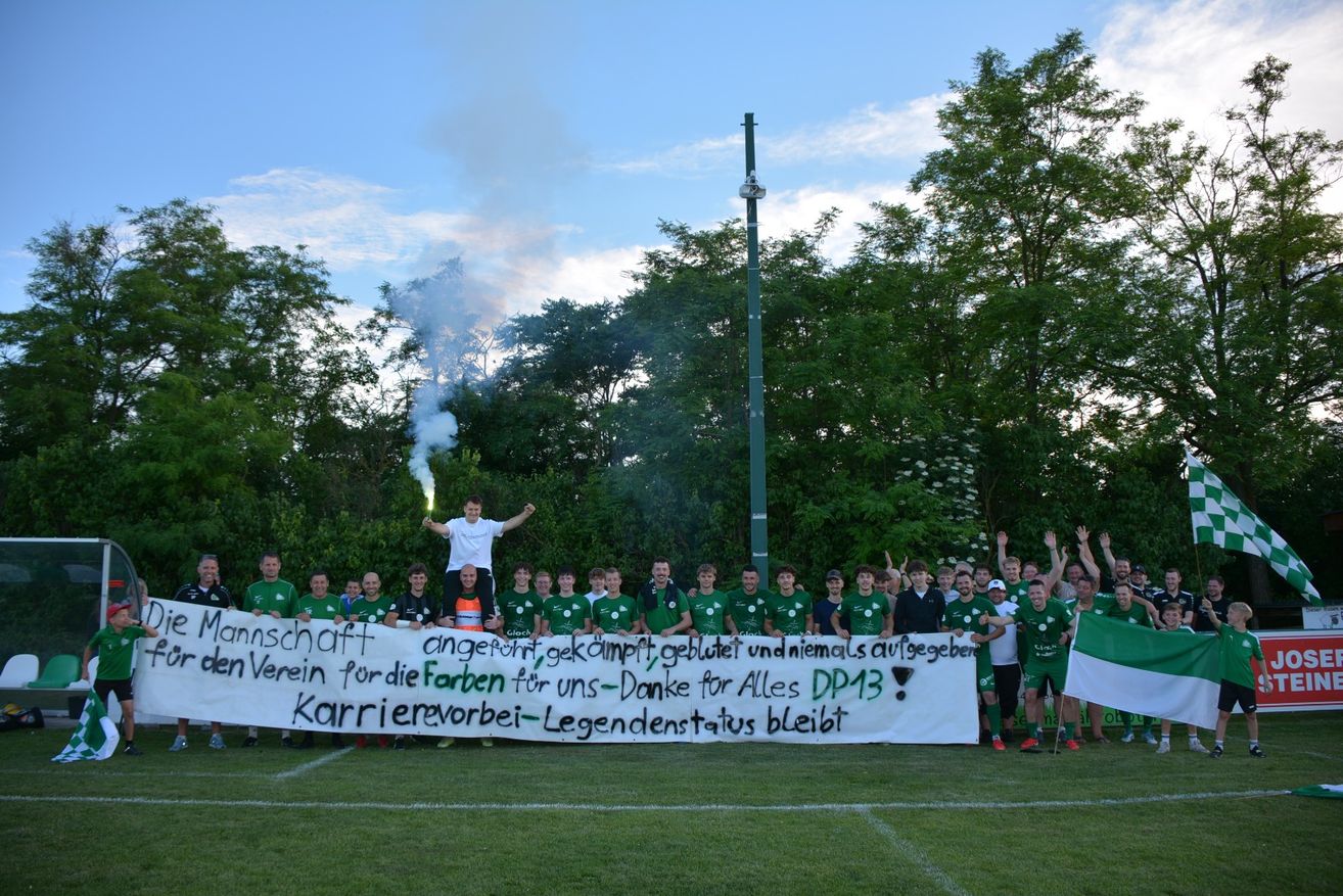 Eine Gruppe von Fußballspielern hält ein Banner mit Raucheffekten. Sie posieren für ein Foto mit Bäumen im Hintergrund.