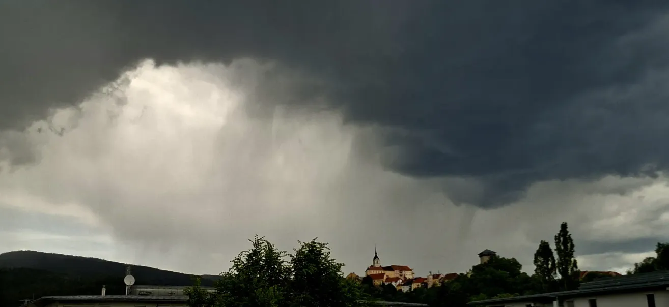 Ein dunkler, bewölkter Himmel über einer Stadt mit einem Kirchturm, es scheint ein starker Regen zu kommen.