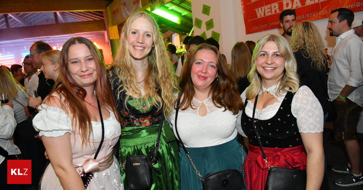 Vier Frauen lächeln in die Kamera, gekleidet in traditioneller deutscher Kleidung, möglicherweise auf einem Festival. Eine trägt ein grünes Kleid, eine andere ein weißes Oberteil und zwei tragen schwarze Oberteile mit roten und grünen Röcken.