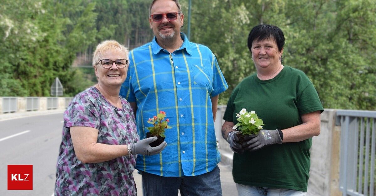 Drei Personen stehen zusammen und halten Pflanzen. Der Mann trägt ein blaues Hemd, die Frau links trägt ein lila Oberteil und die Frau rechts trägt ein grünes T-Shirt. Sie alle lächeln.