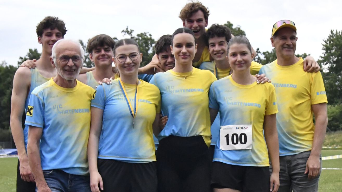 Eine Gruppe von Athleten in gelben und blauen Shirts steht zusammen und lächelt für ein Foto. Sie tragen Medaillen für das Laufen. Das Mädchen auf der rechten Seite hat die Nummer 100 auf ihrem Shirt.