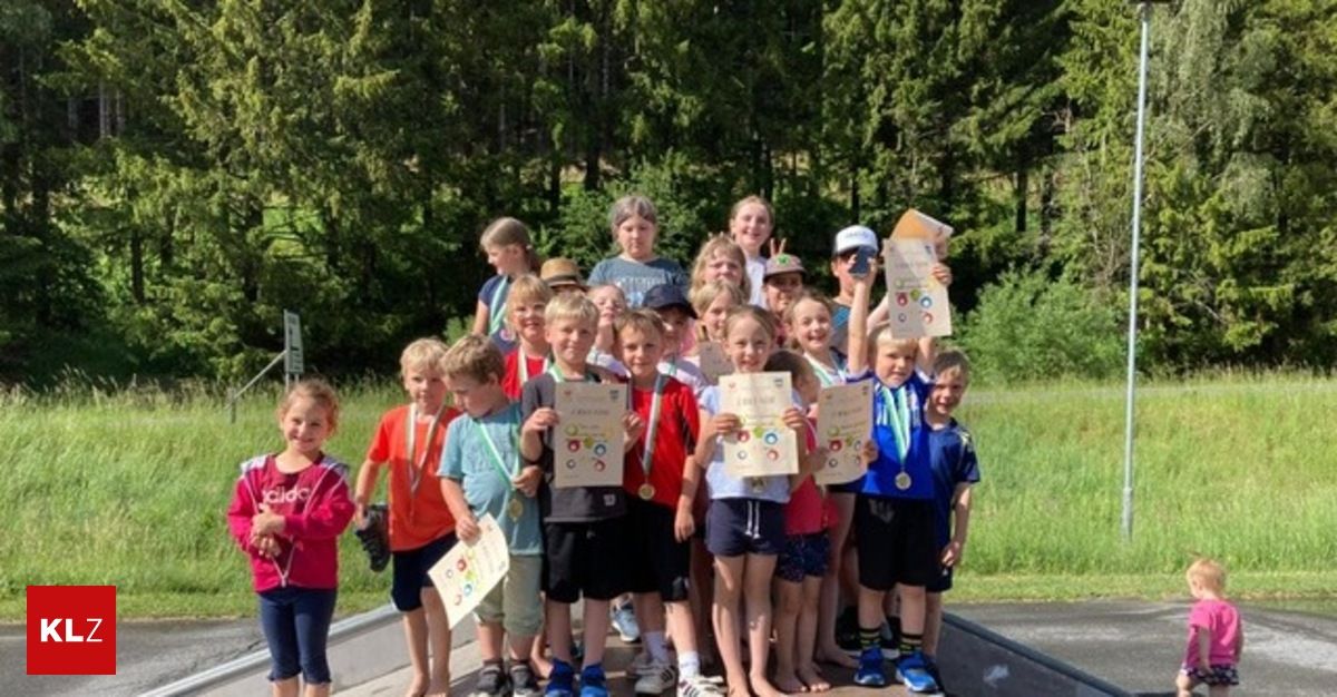 Eine Gruppe von Kindern, wahrscheinlich aus einer Schule, steht in einer Reihe am Straßenrand und hält Medaillen und Urkunden in den Händen. Sie posieren für ein Foto.