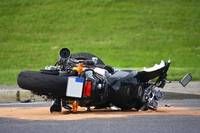 Ein schwarzer Motorrad ist auf der Straße mit einem Grasbereich zerstört. Das Vorderrad ist abgekoppelt. Das Motorrad liegt auf dem Boden.