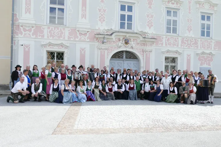 Eine Gruppe von Menschen in traditioneller bayerischer Kleidung, einschließlich Dirndl und Lederhosen, posiert für ein Foto vor einem historischen Gebäude.