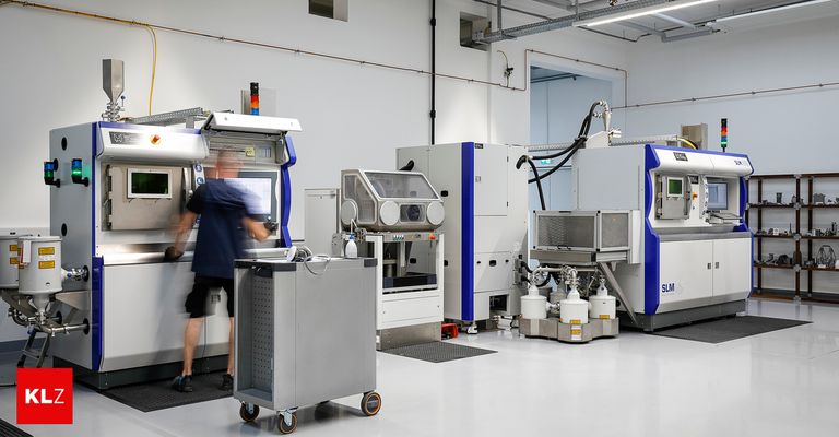 An industrial facility with several machines, a man operates a machine, and others are connected with tubes. The machines are labeled with 'SLM' and have large screens.