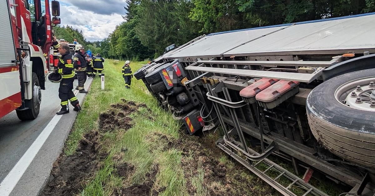 Emergency personnel are responding to a truck accident. The vehicle is overturned on a grassy slope.
