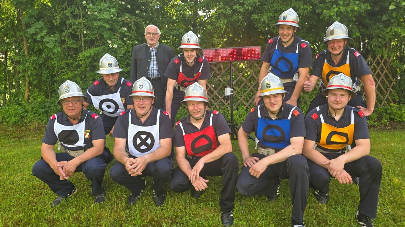Eine Gruppe von Feuerwehrleuten posiert für ein Foto draußen auf einem Rasenfeld mit einem roten LED-Schild im Hintergrund.