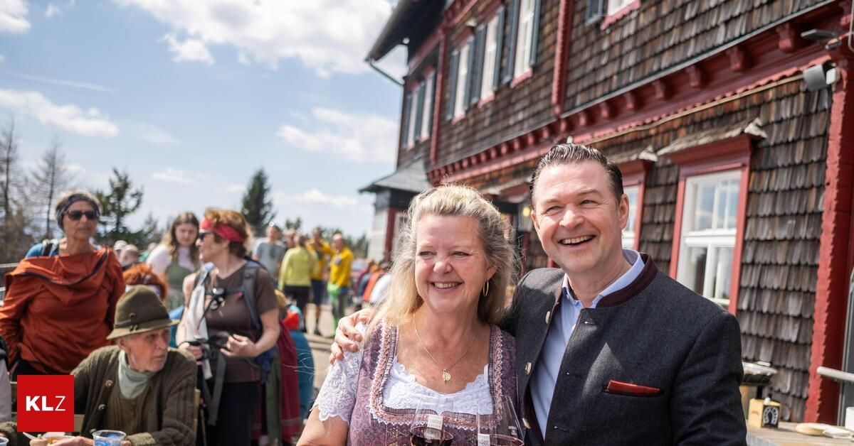 A couple smiling and posing for a photo in front of a building with people walking behind them.