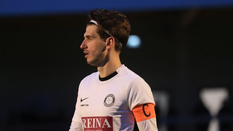 Ein Mann in einem weißen Fußballtrikot mit 'Reina', einem Nike-Logo und einem Kapitänsarmband.
