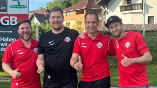 Vier Männer stehen vor einem Haus. Einer trägt ein schwarzes Shirt, zwei tragen rote Shirts und alle haben Nike-Logos. Sie lächeln und posieren für ein Foto.