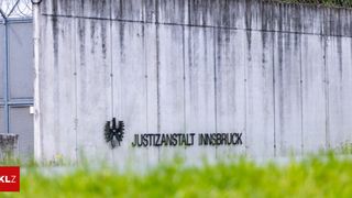 Eine Betonwand mit der Aufschrift 'Justizanstalt Innsbruck' und einem Adlerlogo darüber.