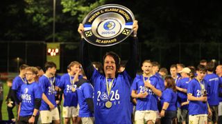 Ein Mann in einem blauen Trikot mit einer goldenen Medaille hält eine silberne Plakette mit der Aufschrift 'Meister 2. Klasse Wechsessel 2025/26'. Er lächelt und wird von Teamkollegen in blauen Trikots umgeben. Sie stehen auf einem Feld unter einem Nachthimmel.