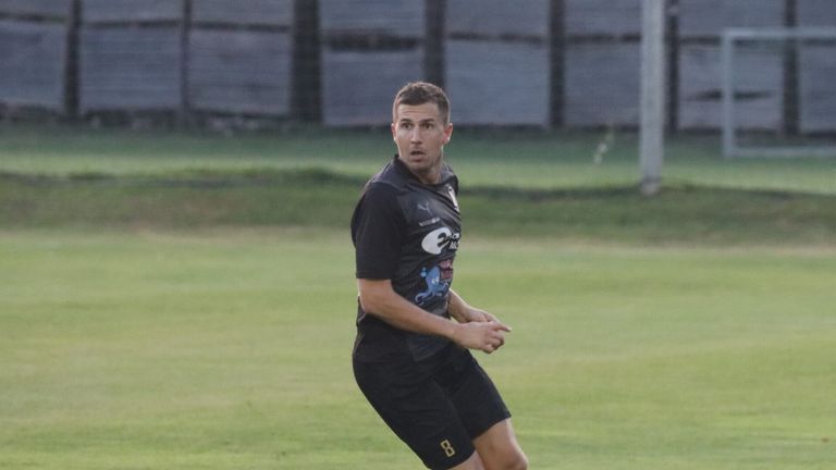Ein Fußballspieler in einem schwarzen Trikot und Shorts läuft auf einem Rasenfeld mit einem unscharfen Hintergrund.