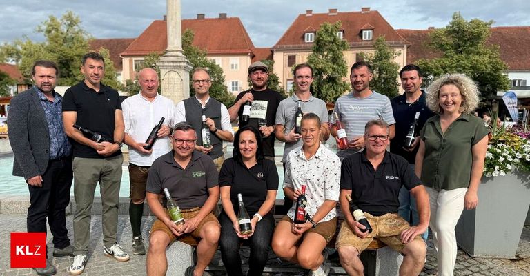 Eine Gruppe von Erwachsenen, sowohl Männer als auch Frauen, posiert vor einem Gebäude für ein Foto und hält Weinflaschen in den Händen.