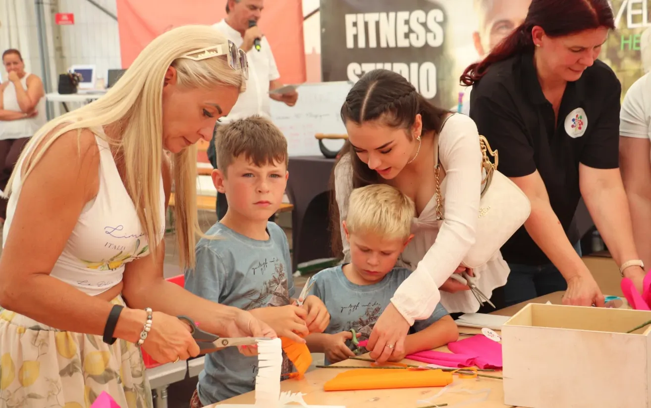 Eine Frau und ein Mädchen bringen zwei Jungen das Schneiden von Papier bei. Die Kinder sitzen mit Papier und Scheren am Tisch.