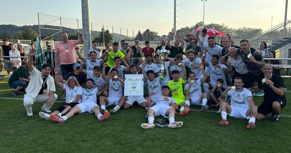 Ein Fußballteam feiert auf einem Feld den Sieg, hält Pokale und Medaillen. Sie posieren für ein Foto mit einem Zertifikat und unter einem roten Schirm.