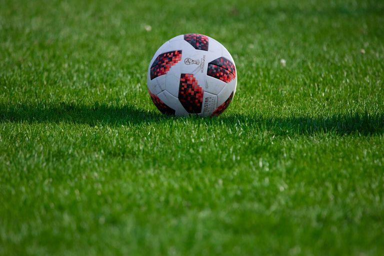 Ein Fußball mit roten und schwarzen Sechsecken liegt auf einem grünen Rasenfeld. Es ist der offizielle Ball für die WM 2018.